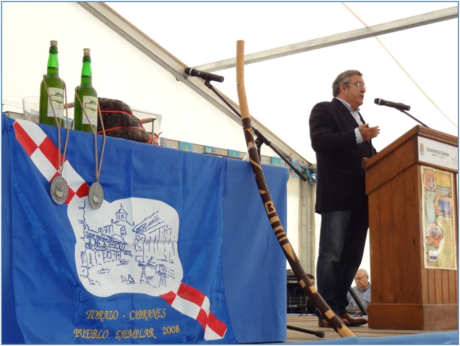 Carlos Cuesta, pronunciando su pregn, con el manjar, la sidra y las medallas en primer plano./ Foto: EL ECO