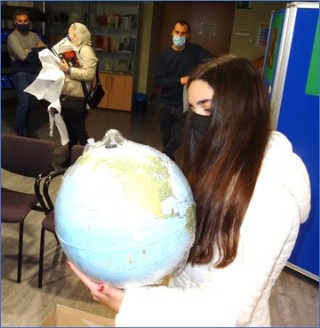 Carla, enfrascada en su globo terrqueo, con el Alcalde, su madre y Gerard al fondo.