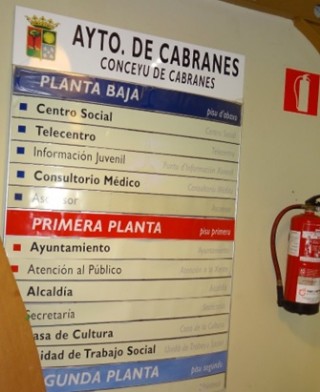Hall de entrada al Ayuntamiento, con el panel informativo en cuya primera línea con fondo azul se dice ´pisu d`abaxo´. Según Alberto, ´esa o final nunca existió en Cabranes´.